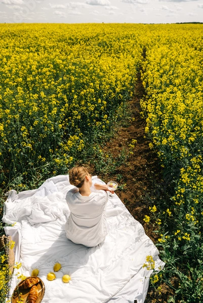 Fototapeta Woman enjoying tea in a yellow flower field on a sunny day in springtime