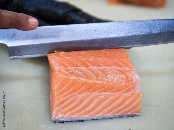 Fototapeta Fresh salmon fillet being sliced with a sharp knife by a chef wearing a black glove. High-quality seafood preparation in a professional kitchen setting.