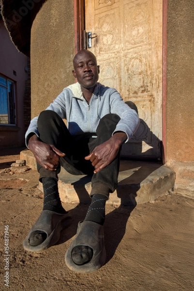 Fototapeta village single african man sited in front of the house in the yard, sunny day