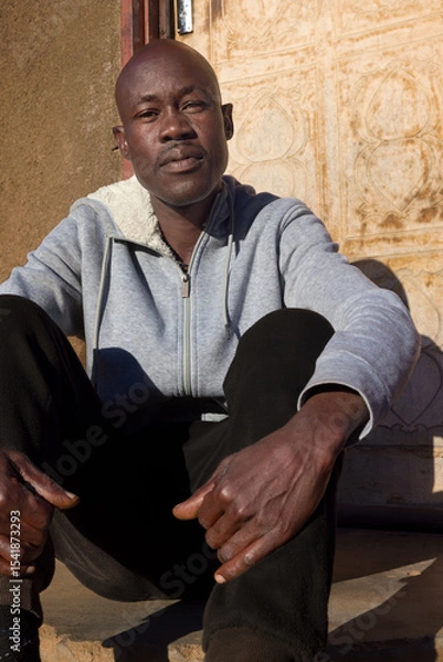 Fototapeta village single african man sited in front of the house in the yard, sunny day