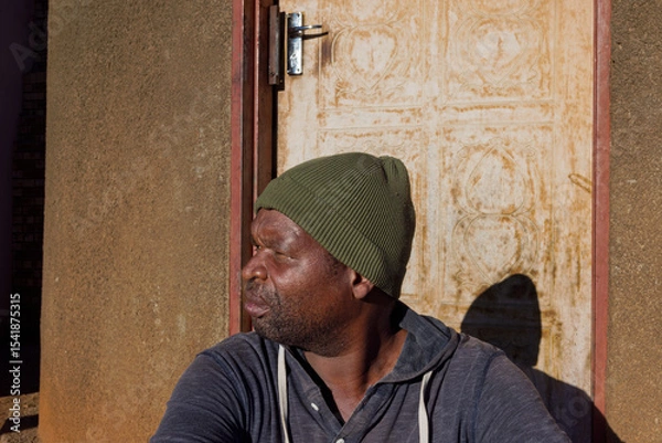 Fototapeta village single african man sited in front of the house in the yard, sunny day