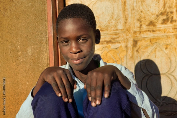 Fototapeta village single african school boy sited in front of the house wearing uniform