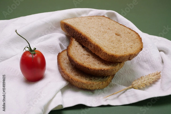 Fototapeta Fette di pane integrale sul tovagliolo, pomodoro e spiga di garno
