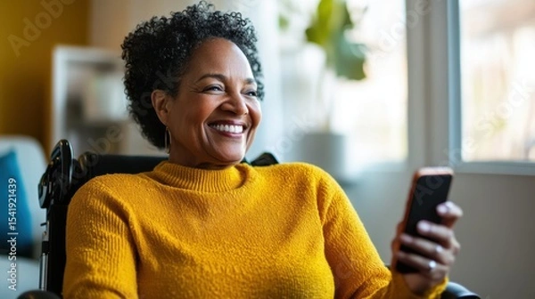 Fototapeta Woman in a yellow sweater smiling while using smartphone in a bright room