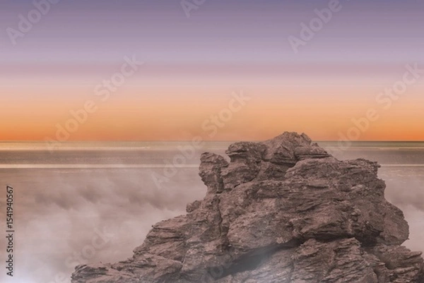 Fototapeta Rugged rock formation is emerging from calm sea in flat design, featuring misty waves, gradient sky