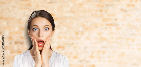 Fototapeta Wow! Excited surprise, expressive happy black hair woman in white shirt. Funny girl with wide open eyes, mouth, hands on cheeks. Shop sales, discounts - ad concept banner image. Bricks wall background