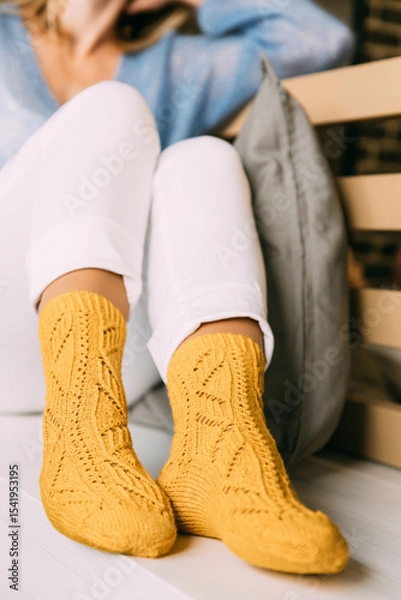Fototapeta Close up of cozy woman in warm yellow knitted winter socks, white trousers and blue warm sweater resting sitting on a bench at cafe in winter time. Lazy day in knitted socks at cafe. Cozy time