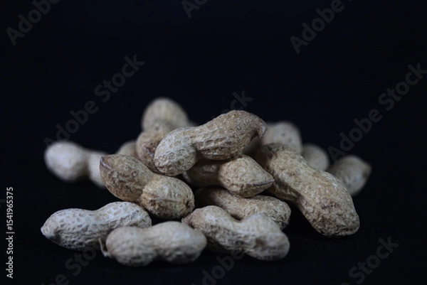 Fototapeta Peanuts on Black: A rustic pile of unpeeled peanuts, still in their shells, rests against a backdrop, showcasing their texture and raw appeal.