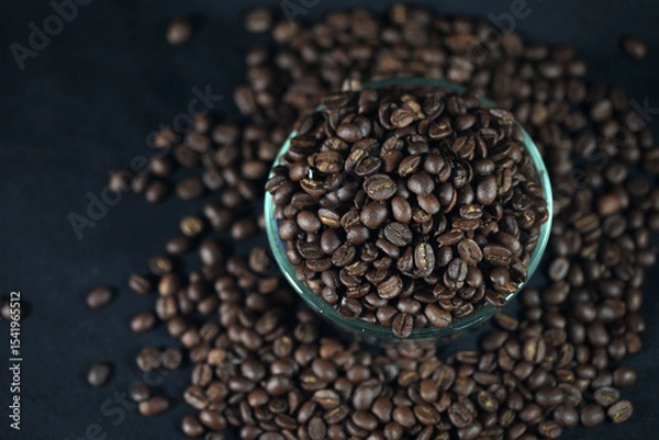 Fototapeta The Essence of Coffee: A detailed capture of rich, roasted coffee beans piled into a glass bowl, and spread around. this image conveys the essence of an energizing beverage.