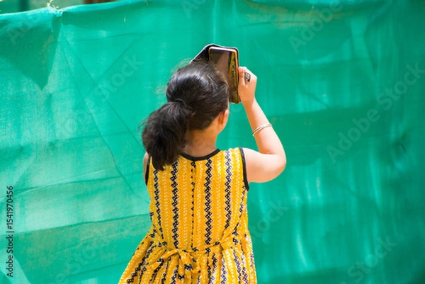 Obraz young school girl in yellow frock taking bird photo using mobile phone. childhood curiosity, digital learning, and joy of exploring nature. themes of technology, childhood, education, creativity. 
