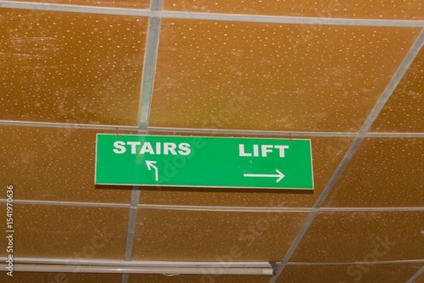 Obraz green ceiling-mounted indicator board displaying directional arrows for stairs (left) and lift (right), commonly seen in hospitals, malls, office buildings, and public infrastructure