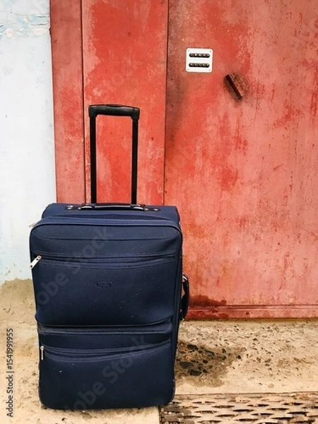 Obraz Travel suitcase placed beside an old weathered door