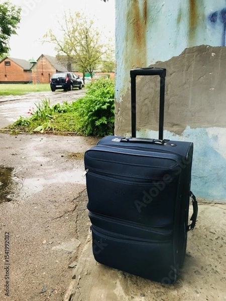 Obraz Travel suitcase resting against a weathered wall outside