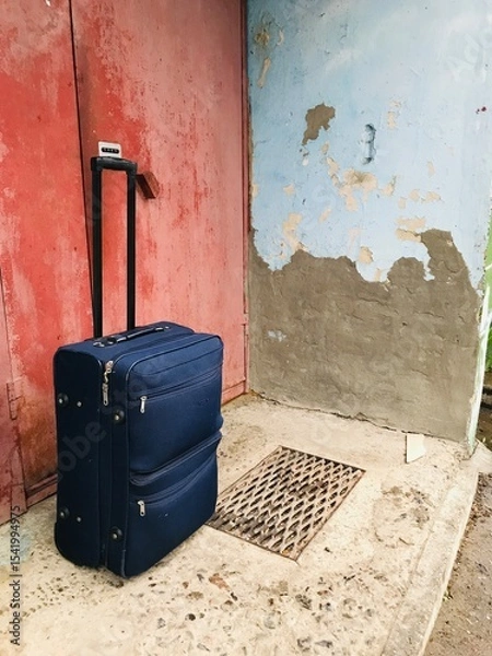 Obraz Travel suitcase resting against a weathered wall outside