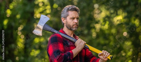 Obraz Lumberjack men in forest with axe. Lumberjack carries axe. Handsome man with axe. Lumberjack in woods with an ax. Lumberjack in shirt with heavy axe. Strong man work in forest. Focused expression