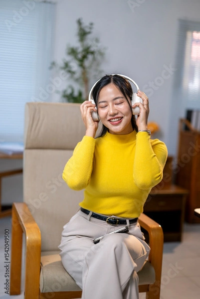 Fototapeta A woman in a yellow shirt is sitting in a chair and listening to music