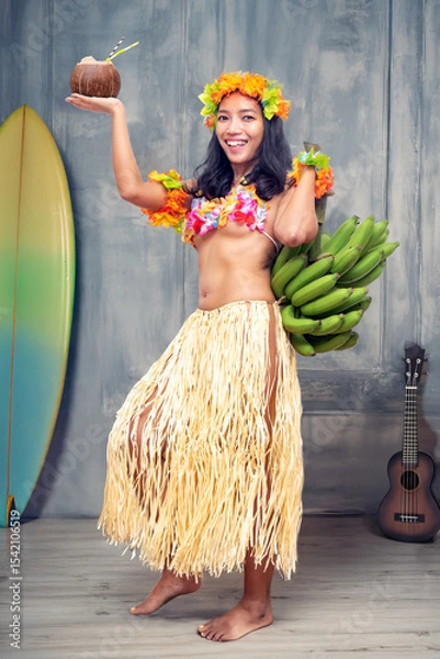 Obraz Ethnic cheerful woman in traditional Hawaiian costume holding a bunch of bananas and a coconut drink in an older studio with props