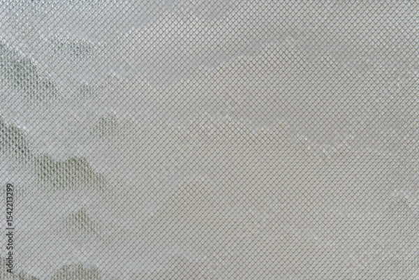 Fototapeta Water streams down glass covered with metal mesh, catching light and texture. The effect is cool, modern, and quietly captivating.