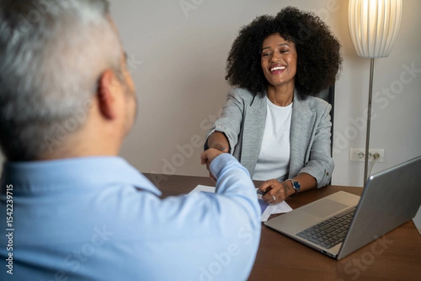 Fototapeta Happy mid aged business woman manager handshaking greeting client in office. Smiling female executive making successful deal with partner shaking hand at work at meeting table. 