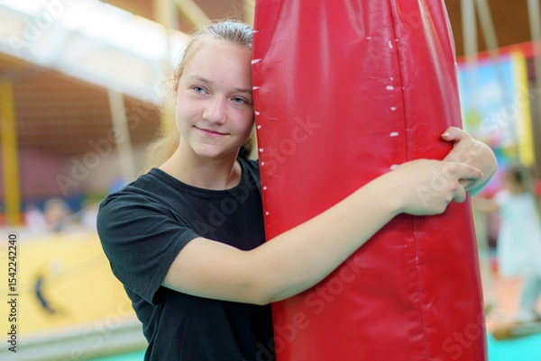 Obraz Girl enjoying gymnastic practice while hugging a red safety mat in a training facility during afternoon hours