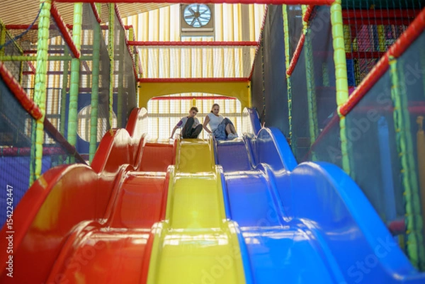 Obraz Kids enjoy playful fun sliding down colorful slides in a vibrant indoor playground during afternoon hours
