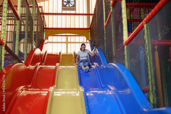 Obraz Colorful indoor playground features a girl sliding down bright slides in the afternoon