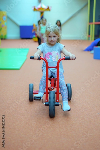 Obraz Child enjoys riding a red tricycle in an indoor play area on a bright afternoon