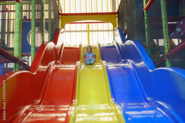 Obraz Child slides down colorful play structure in indoor playground during afternoon fun