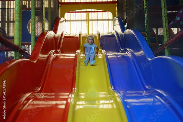 Fototapeta Child enjoys sliding down colorful play structure in indoor playground during afternoon
