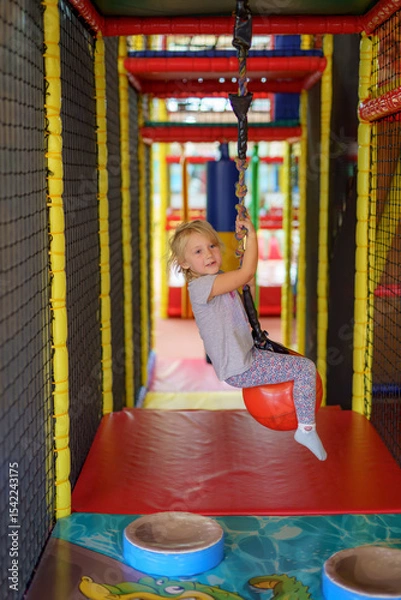 Obraz Young girl enjoys swinging on a colorful playground zip line at an indoor play area during afternoon fun time