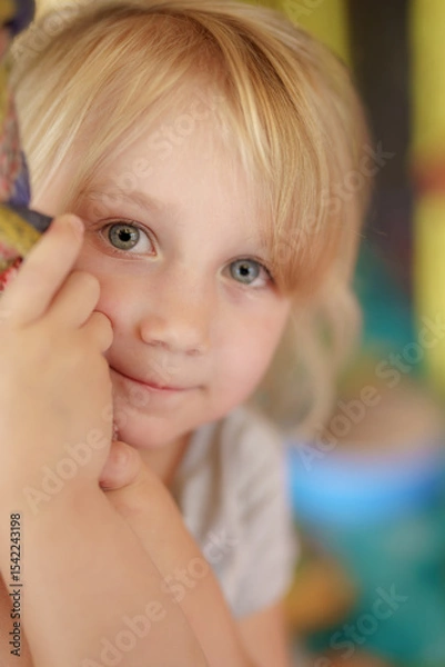 Obraz Young child with blonde hair smiling while holding onto a colorful structure in a playful environment