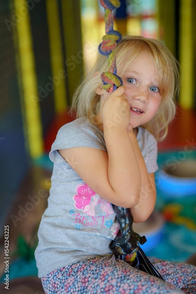 Obraz Child enjoys swinging indoors at a colorful play area with soft flooring and various toys available
