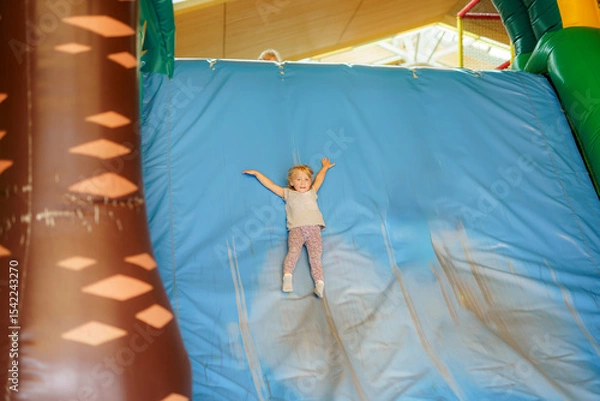 Obraz Child joyfully sliding down an inflatable slide in a playful indoor playground during daytime fun activities