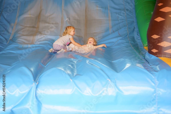 Obraz Children play joyfully on a large inflatable slide at a birthday party indoors during the afternoon