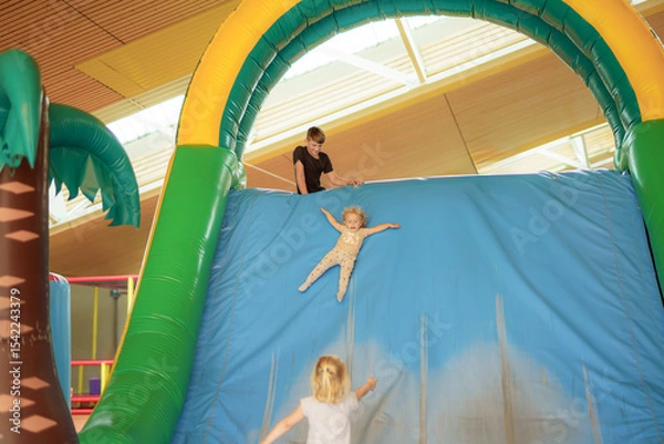 Obraz Children enjoy sliding down a large inflatable structure in a brightly lit indoor play area during a fun recreational day