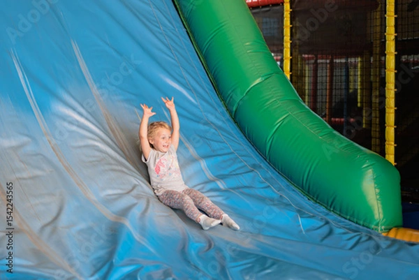 Obraz Child joyfully sliding down a colorful indoor playground slide during a fun-filled play session at a family entertainment center