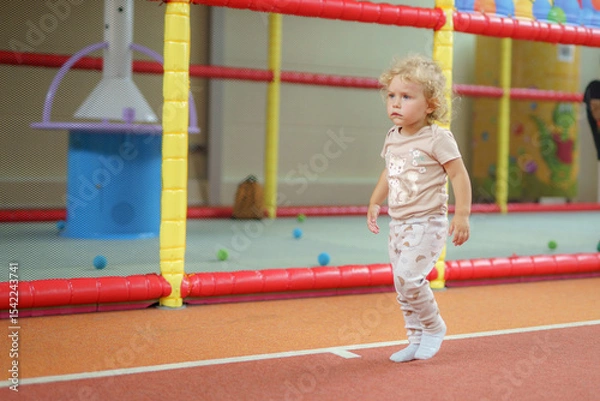 Obraz Young child enjoying active playtime in a colorful indoor play area with soft surfaces and safety barriers during the daytime
