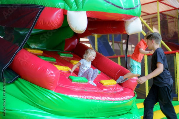 Obraz Kids enjoying fun at a colorful inflatable play structure in an indoor amusement center during a sunny afternoon