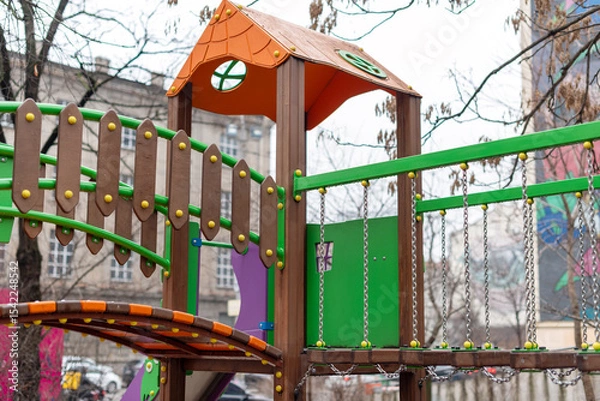 Fototapeta Vibrant children's playground equipment featuring climbing elements, bridges, and slides, offering fun and adventure within a dynamic urban area setting.