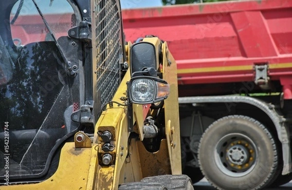 Fototapeta Headlight of a mini loader close up with a blurry truck in the background. selective focus of construction equipment