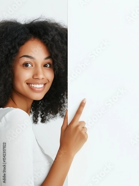 Obraz Smiling woman with curly hair pointing to a blank wall in a bright indoor space during daylight