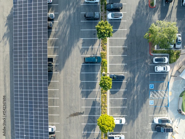 Fototapeta Aerial view of solar panels installed as shade roof over parking lot for parked cars. Photovoltaic technology integrated in urban infrastructure. High quality photo