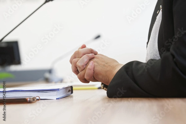 Obraz Close-up of clasped hands resting on a desk during a business meeting, conveying tension and nervous anticipation; for use in articles or presentations about negotiation stress. Photo