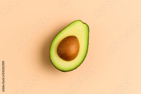Fototapeta Top view of a sliced ripe avocado showing the seed, placed on a soft peach-colored background..