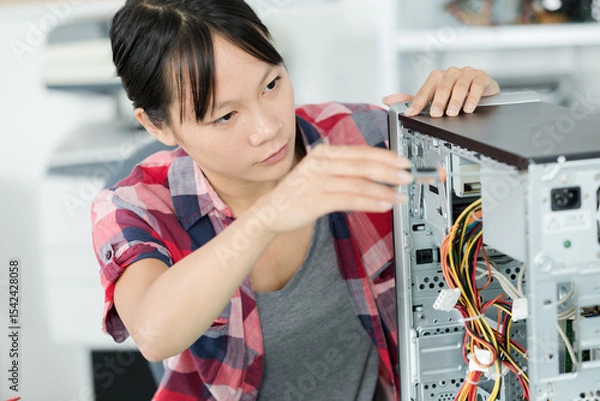 Obraz young woman fixing a desktop computer seated at a table