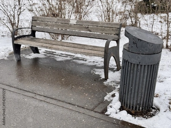 Obraz A Snowy Park Bench Alongside a Trash Can Set in a Beautiful Winter Landscape Scene. A serene snowy park scene depicting a wooden bench alongside a sleek, modern trash can, creating environment