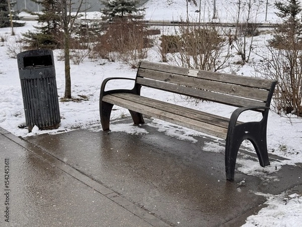 Obraz A Snowy Park Bench Alongside a Trash Can Set in a Beautiful Winter Landscape Scene. A serene snowy park scene depicting a wooden bench alongside a sleek, modern trash can, creating environment