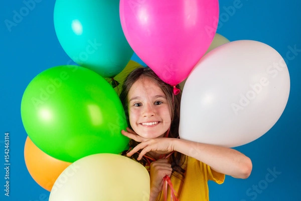 Obraz Birthday, party or celebration concept. Cute little european smiling girl makes her way through the balloons on blue background