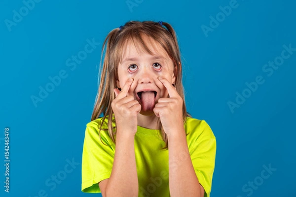 Obraz Happy funny young blonde girl posing, fooling around and showing tongue against blue background