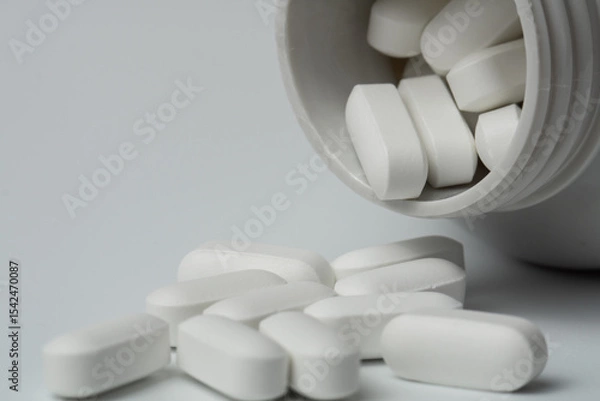 Fototapeta White pills tablets spilled from a bottle on a light grey background close up